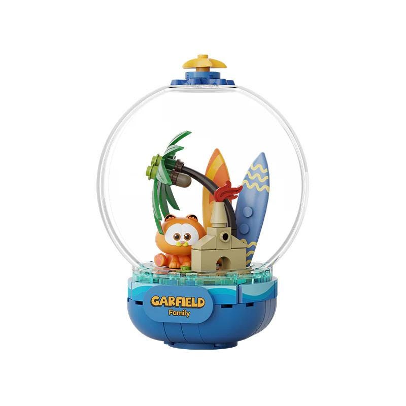 A toy figurine of a cat inside a glass globe, surrounded by various beach-themed objects such as a surfboard, palm tree, and sand castle.