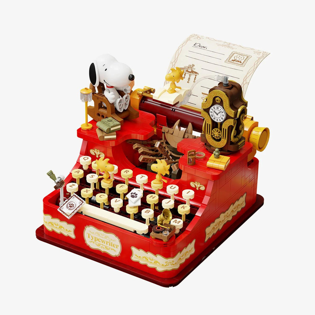 A red and gold toy typewriter with various small figures and objects, including a clock, a letter, and a Snoopy figurine.