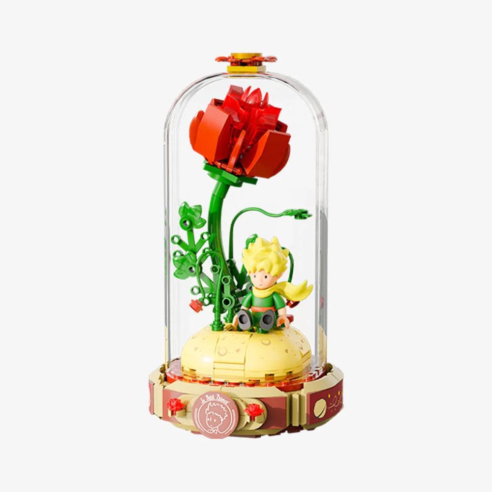 A Lego figurine of a young boy sitting on a yellow base, surrounded by a glass dome containing a red flower and green plants.