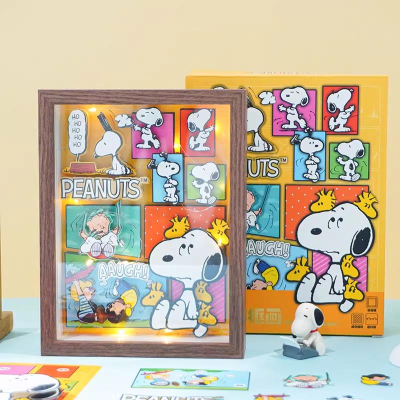 a framed collage of various Peanuts characters, including Snoopy, Woodstock, and other iconic figures from the Peanuts comic strip. The collage is displayed on a table, with a small Peanuts-themed toy figurine placed next to it.