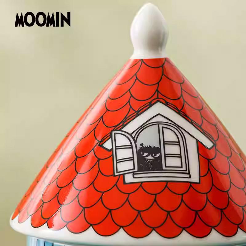 a ceramic object with a red and white pattern resembling a house or a roof, with a small cat depicted inside the window.