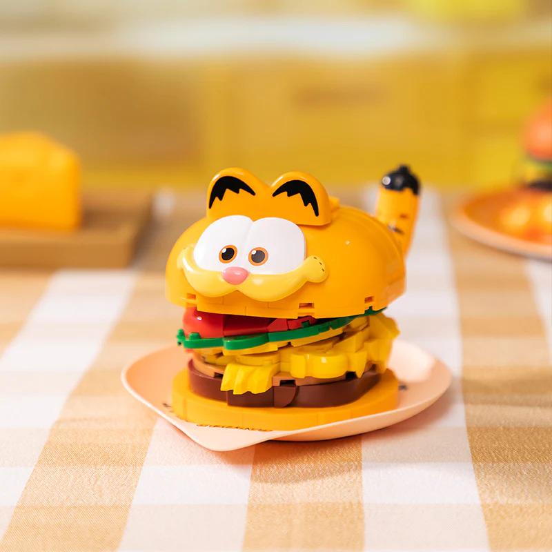 A yellow toy resembling a hamburger with a cat face design sits on a plate.