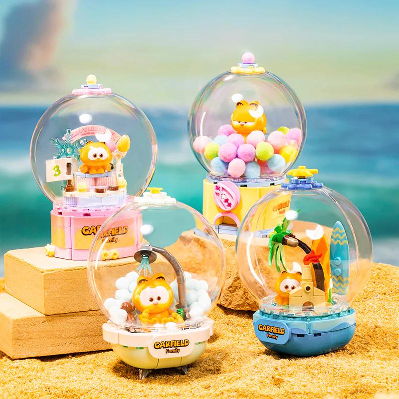 four colorful, whimsical toy figurines of the popular cartoon character, Garfield, displayed on a sandy surface.