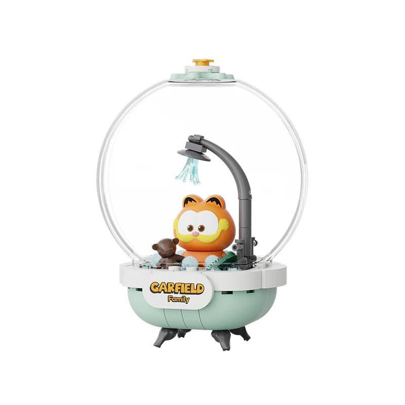A toy figurine of a cat, resembling the character Garfield from the animated television series, is sitting in a bathtub with a shower head above it.