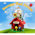 A Lego model of a red house with a glass dome containing a Snoopy figurine and a sunflower, set against a blue sky with clouds.