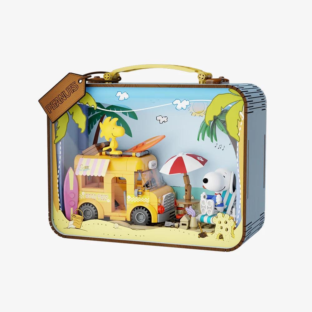 A Peanuts-themed toy box with a yellow toy truck, a yellow toy bus, and a toy character from the Peanuts series. The toy box is decorated with a beach scene, including a palm tree, an umbrella, and a surfboard.