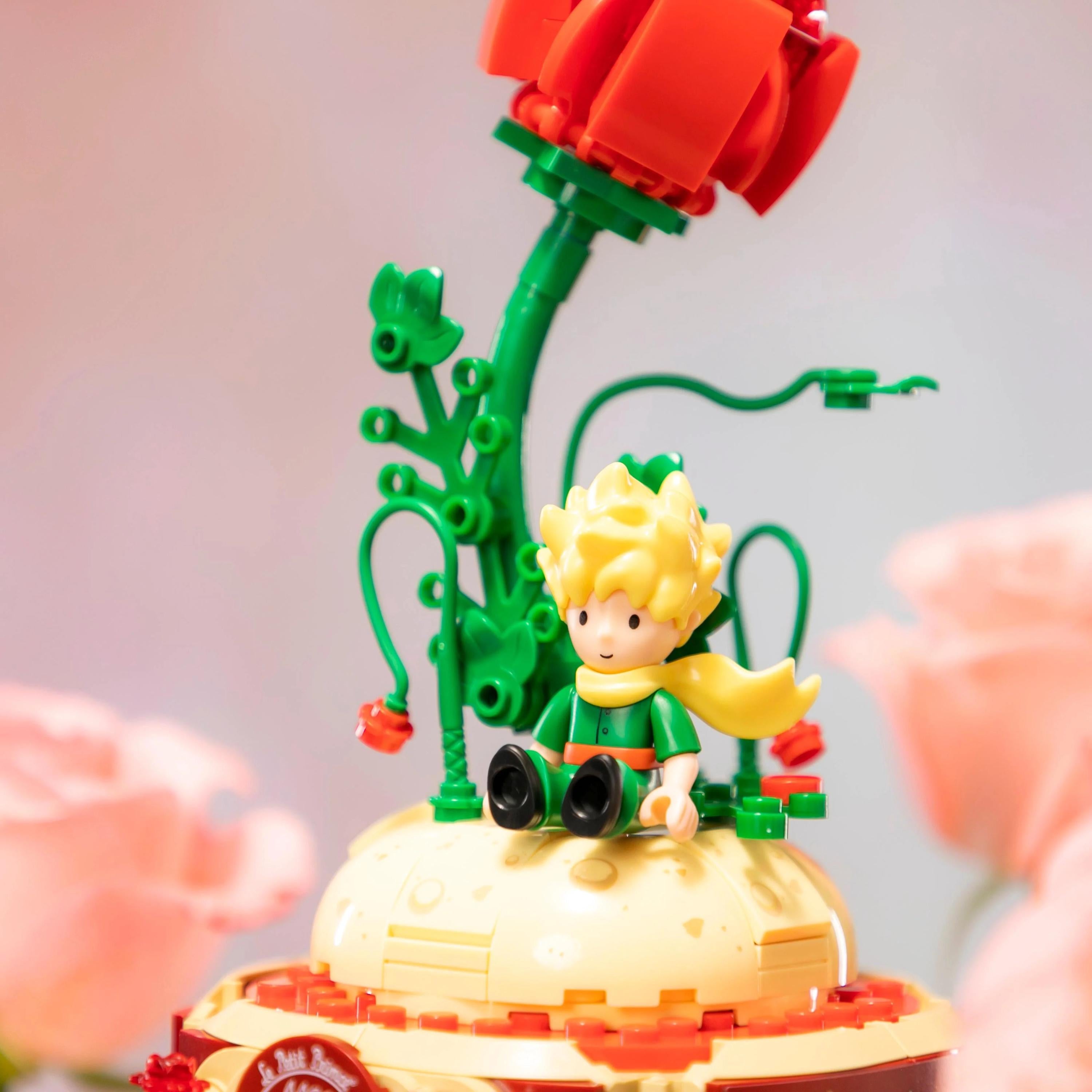 A toy figurine of a young boy sitting on a yellow base, with a large red flower-like structure on top.