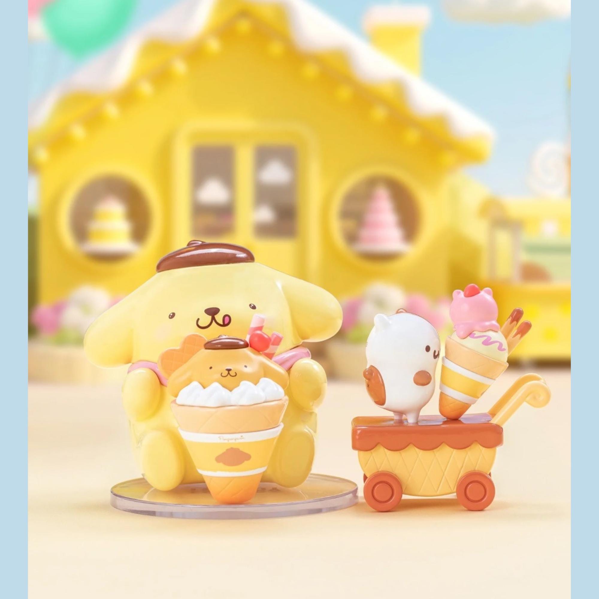 A yellow toy figurine is sitting on a table, holding a cupcake, with a small white figurine and a pink figurine on a cart behind it. In the background, there is a yellow house with a yellow roof and a pink tree.