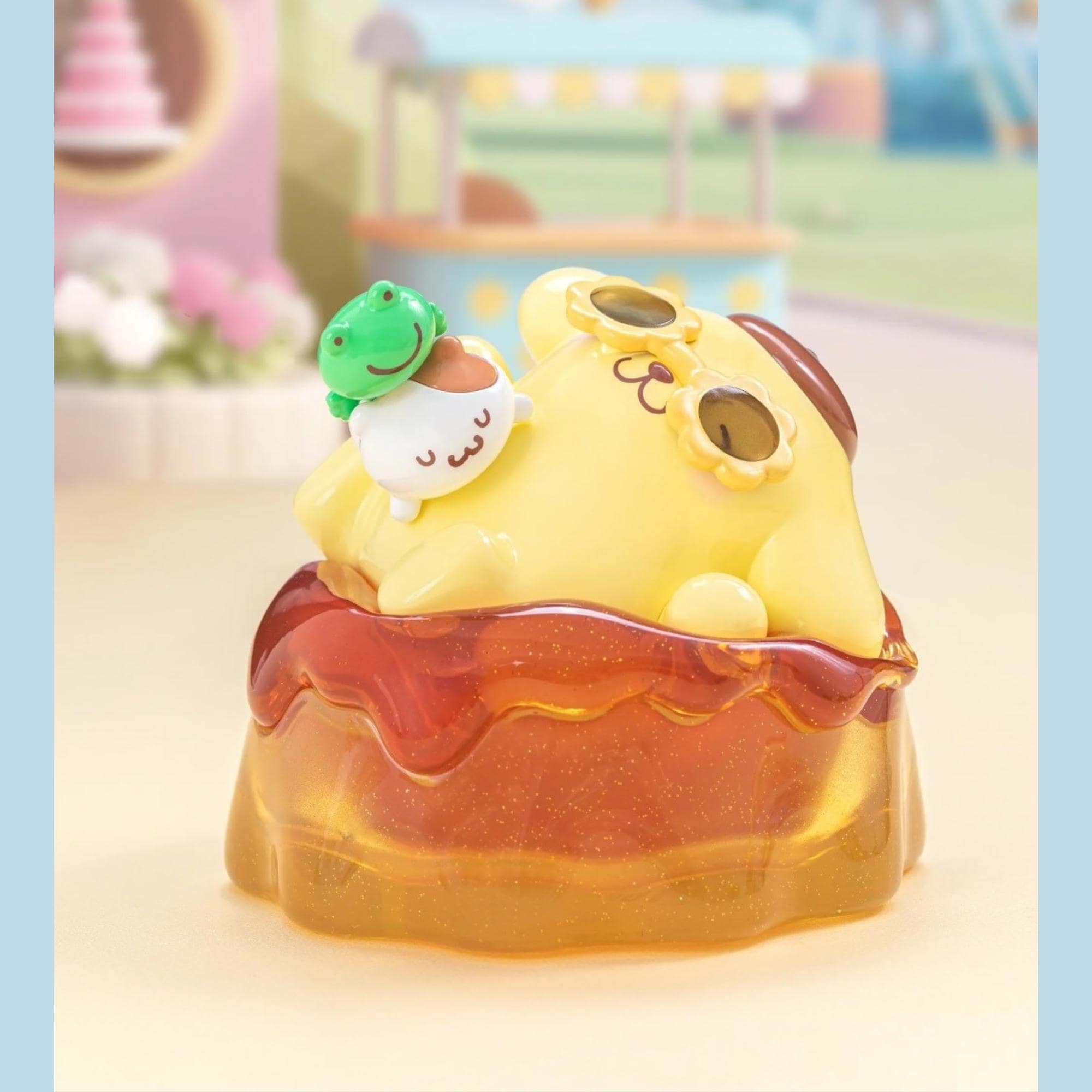 A yellow toy figurine with a green frog on top, sitting on a red and yellow jelly-like object, with a blurred background that appears to be a colorful, whimsical scene.