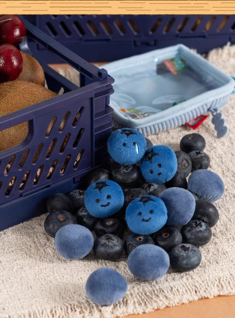 a collection of blueberries and kiwis, with some of the blueberries having faces drawn on them. The blueberries are scattered on a surface, and there are also some blueberries placed in a blue plastic crate.