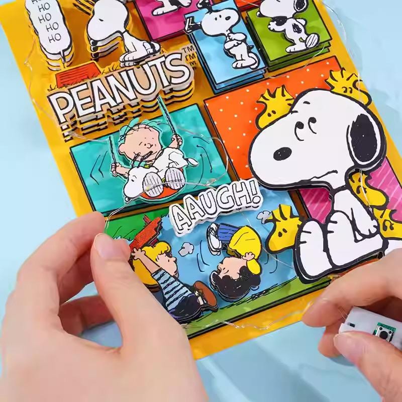 A person's hands are holding a colorful Peanuts-themed puzzle or book, featuring various Peanuts characters and scenes.