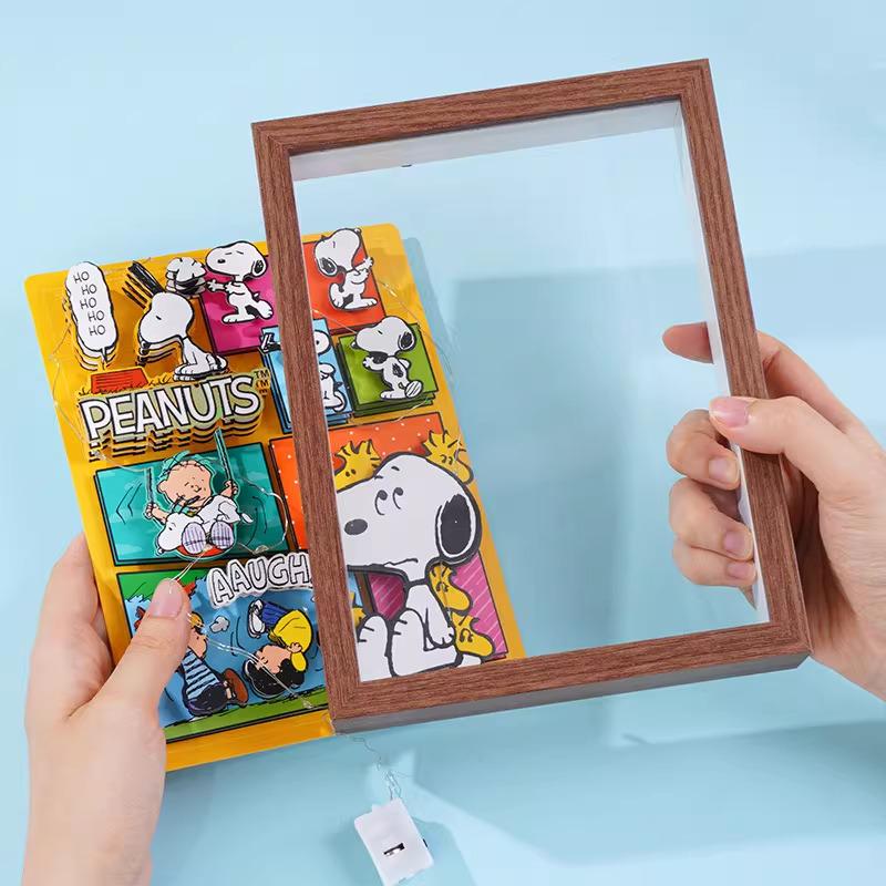 A person's hands holding a wooden frame with a colorful Peanuts comic book featuring Snoopy and other characters.