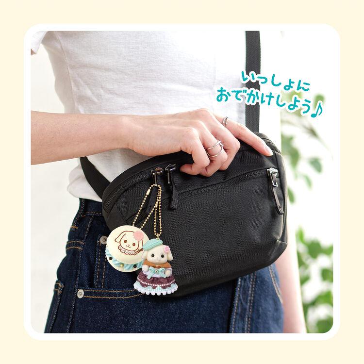A person wearing a white shirt and blue jeans is holding a black bag with a charm attached to it.