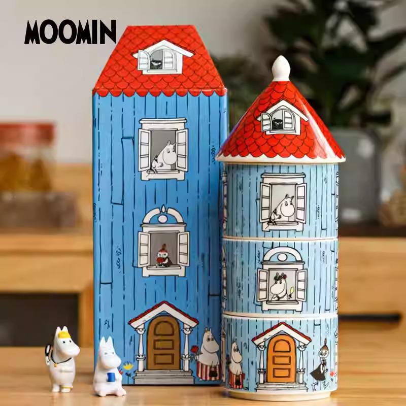 A blue toy house with a red roof, along with a cylindrical container and two small figurines, all set against a blurred background.
