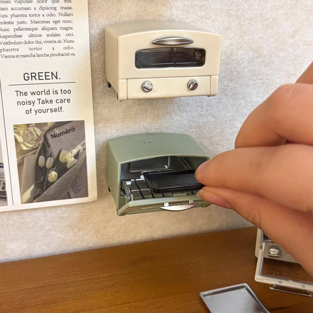 A person's hand is holding a small green toaster oven, which is mounted on a wall.