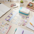 a desk with various office supplies and craft materials, including a notebook, pens, stickers, and a printer.