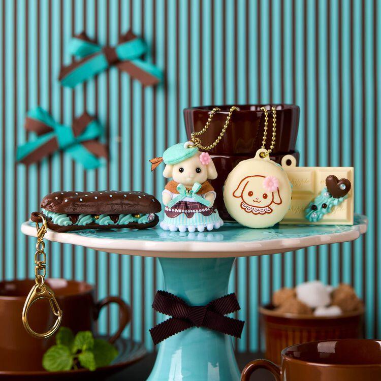 A collection of decorative items, including a small figurine, a chocolate pastry, and a keychain, displayed on a blue and white striped cake stand.