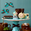 A collection of decorative items, including a small figurine, a chocolate pastry, and a keychain, displayed on a blue and white striped cake stand.