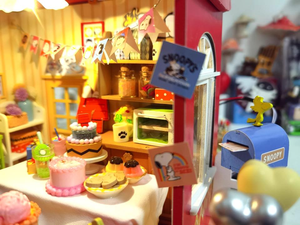 A miniature diorama depicting a bakery scene with various desserts, decorations, and a Snoopy figurine.
