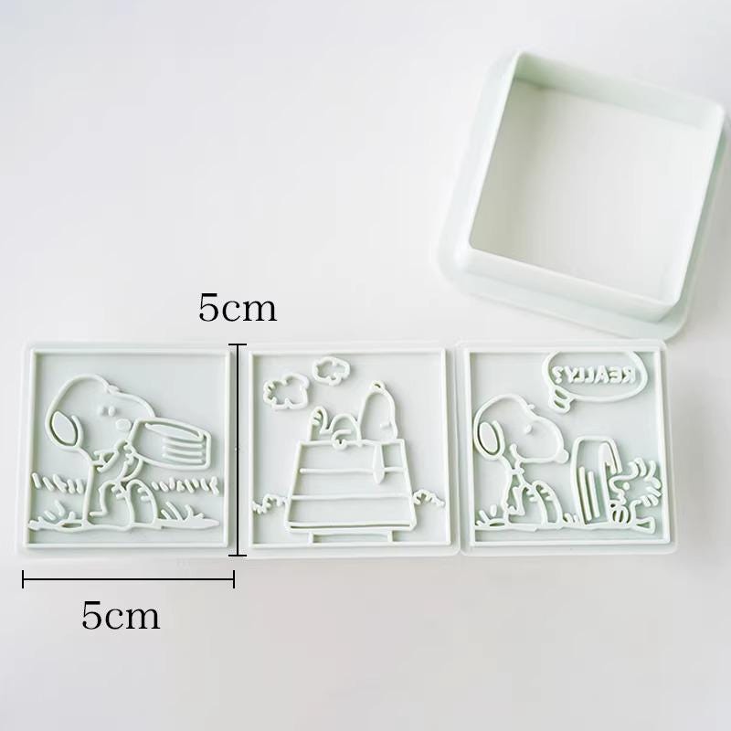 three square cookie cutouts of characters from the Peanuts comic strip, including Snoopy, Woodstock, and Charlie Brown.