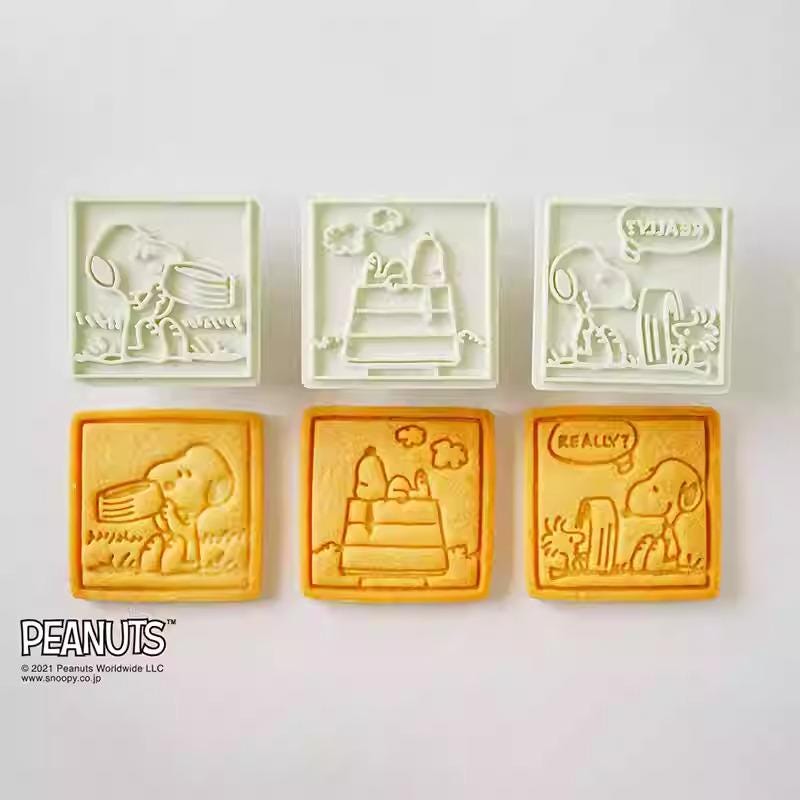 six square cookie cutters shaped like characters from the Peanuts comic strip, including Snoopy, Woodstock, and other iconic figures.