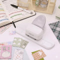 a variety of craft supplies, including a hole puncher, a notebook, and several colorful fabric pieces, all arranged on a desk.