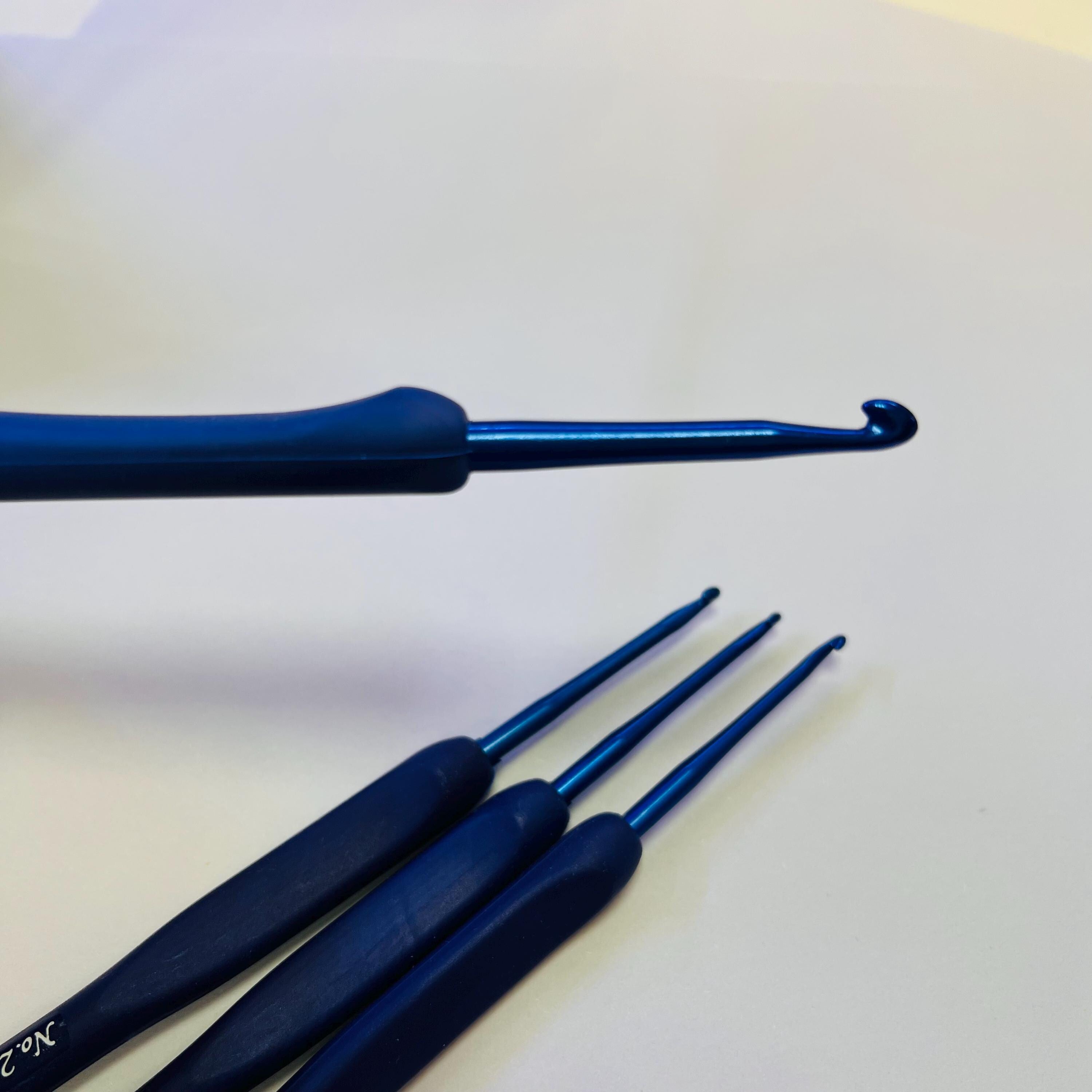 A close-up image of a crochet hook with a blue handle and three blue crochet hooks arranged on a white surface.