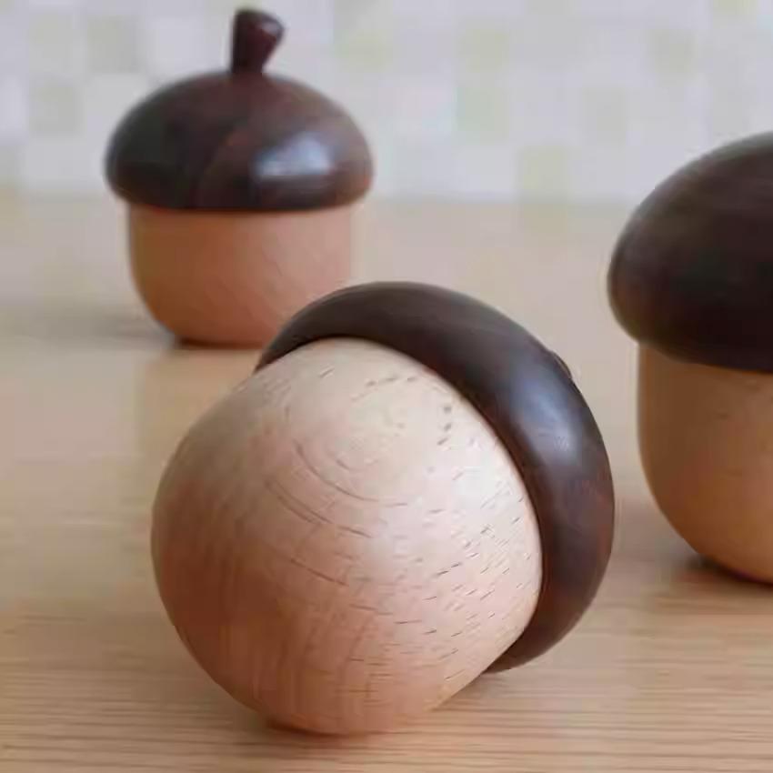 three wooden acorn-shaped objects with dark brown caps, arranged on a wooden surface.