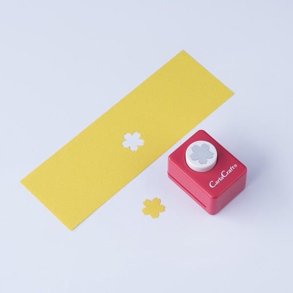 a yellow paper with two white flower-shaped cutouts and a red paper punch with a white flower-shaped cutout on top.