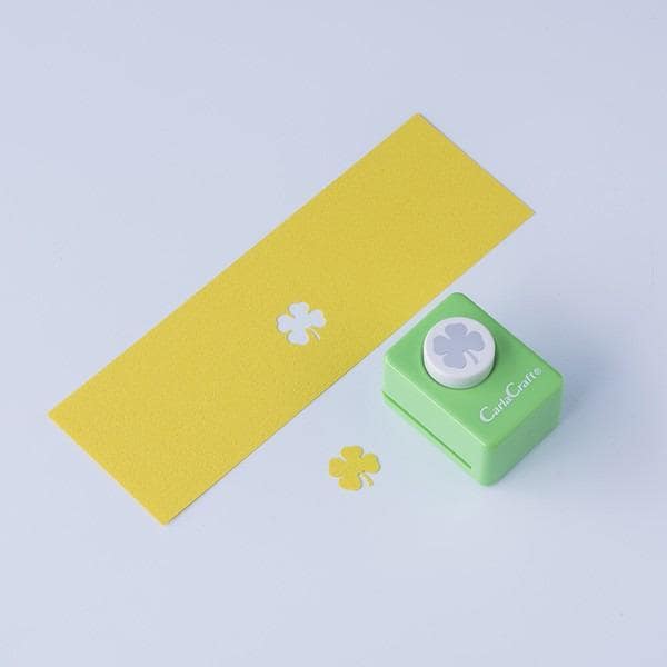 a yellow paper with two white clovers and a green paper punch with a white clover design on it, all placed on a white background.