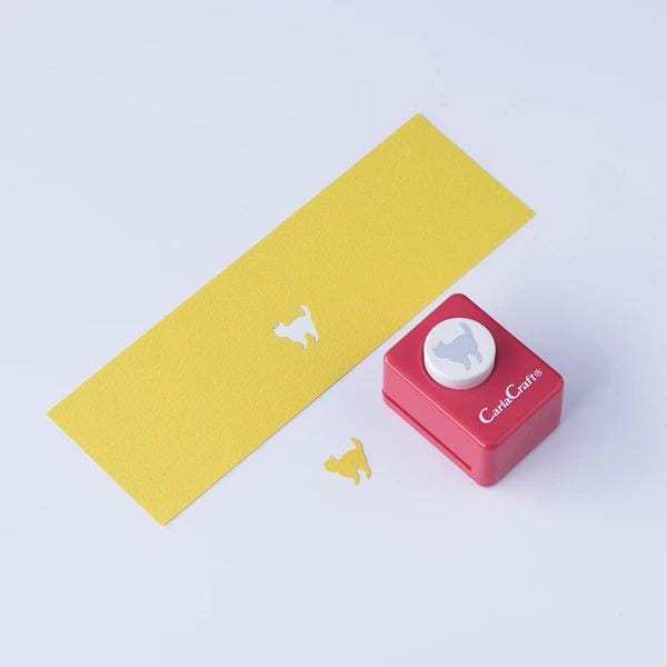 a yellow paper with a white cat silhouette and a red push button cutter with a white cat silhouette on it, along with a yellow paper with a white cat silhouette.