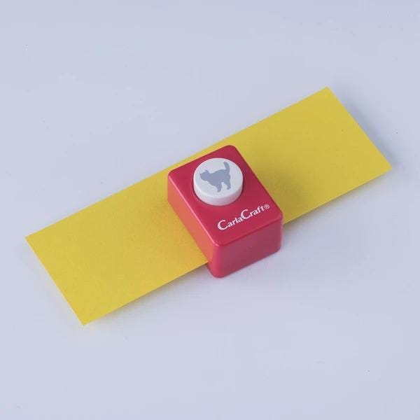A red and yellow paper punch with a white cat silhouette on it, placed on a yellow surface.
