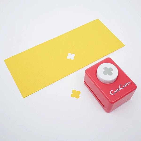 a yellow paper with a white flower design and a red and white craft punch with a hole in the center, both placed on a white background.