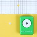 A green push button hole puncher is placed on a yellow background, with a grid pattern visible in the background.