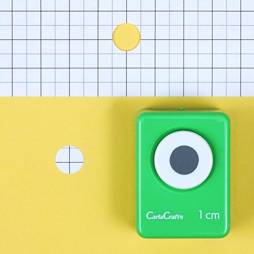 A green hole puncher is placed on a yellow background, with a grid pattern visible in the background.