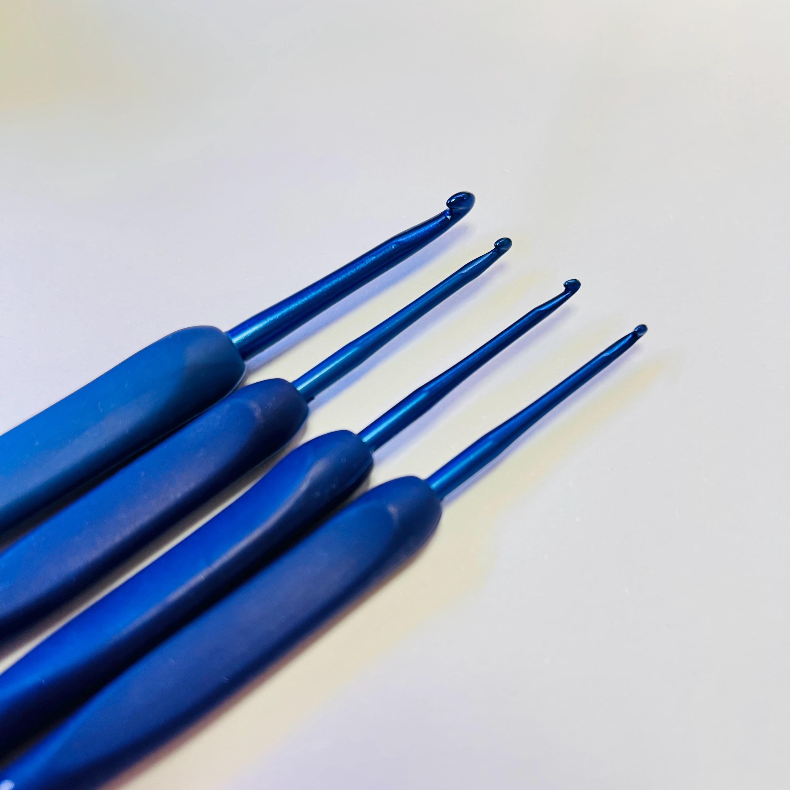 A close-up image of four blue crochet hooks arranged in a row on a white background.