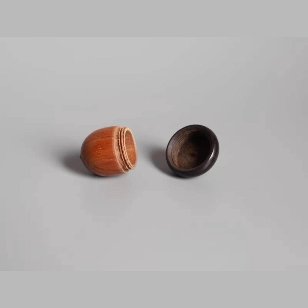 a wooden object with a round shape, possibly a ball or a container, and a black object with a similar round shape, possibly a lid or a container, placed on a plain background.