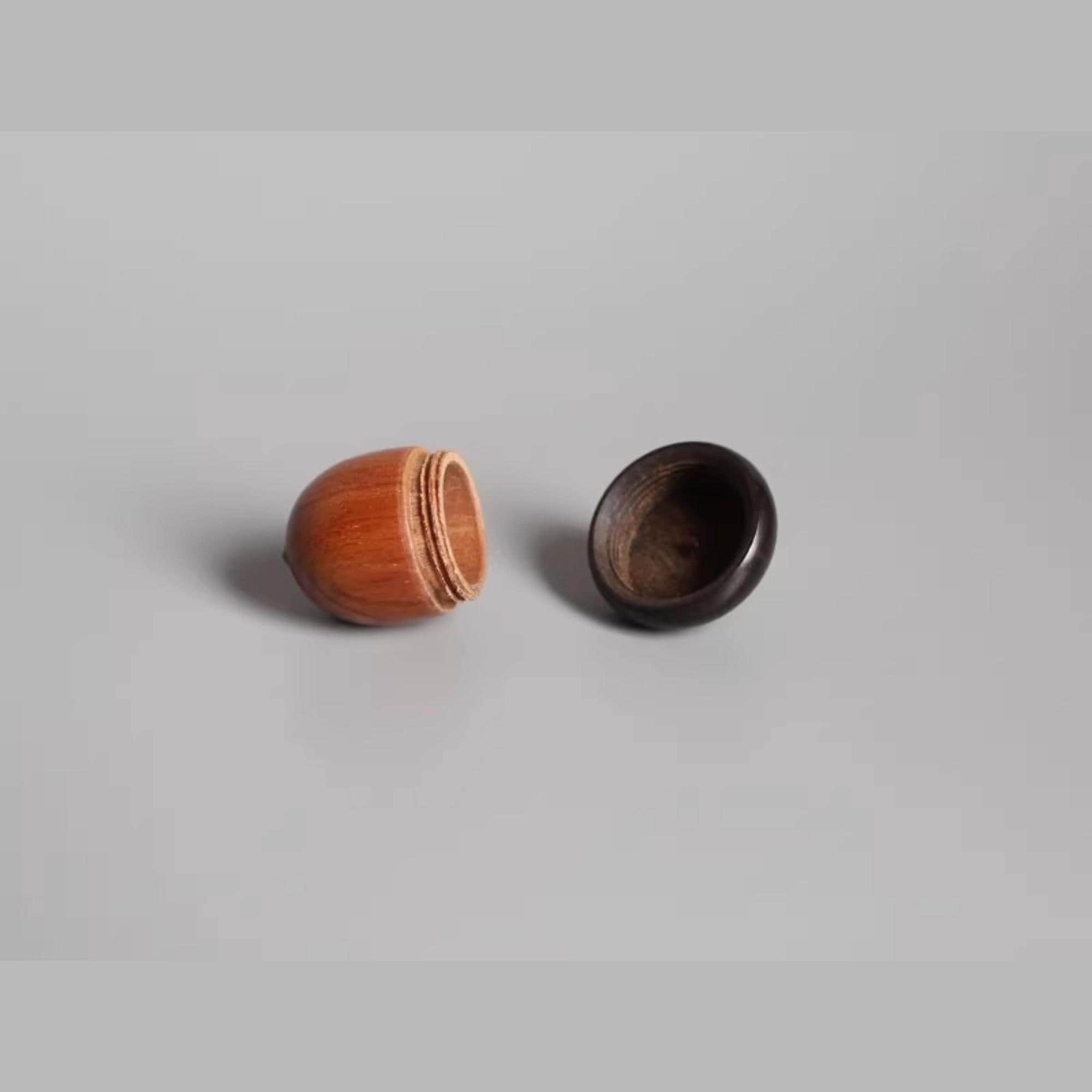 a wooden object with a round shape, possibly a ball or a container, and a black object with a similar round shape, possibly a lid or a container, placed on a plain background.