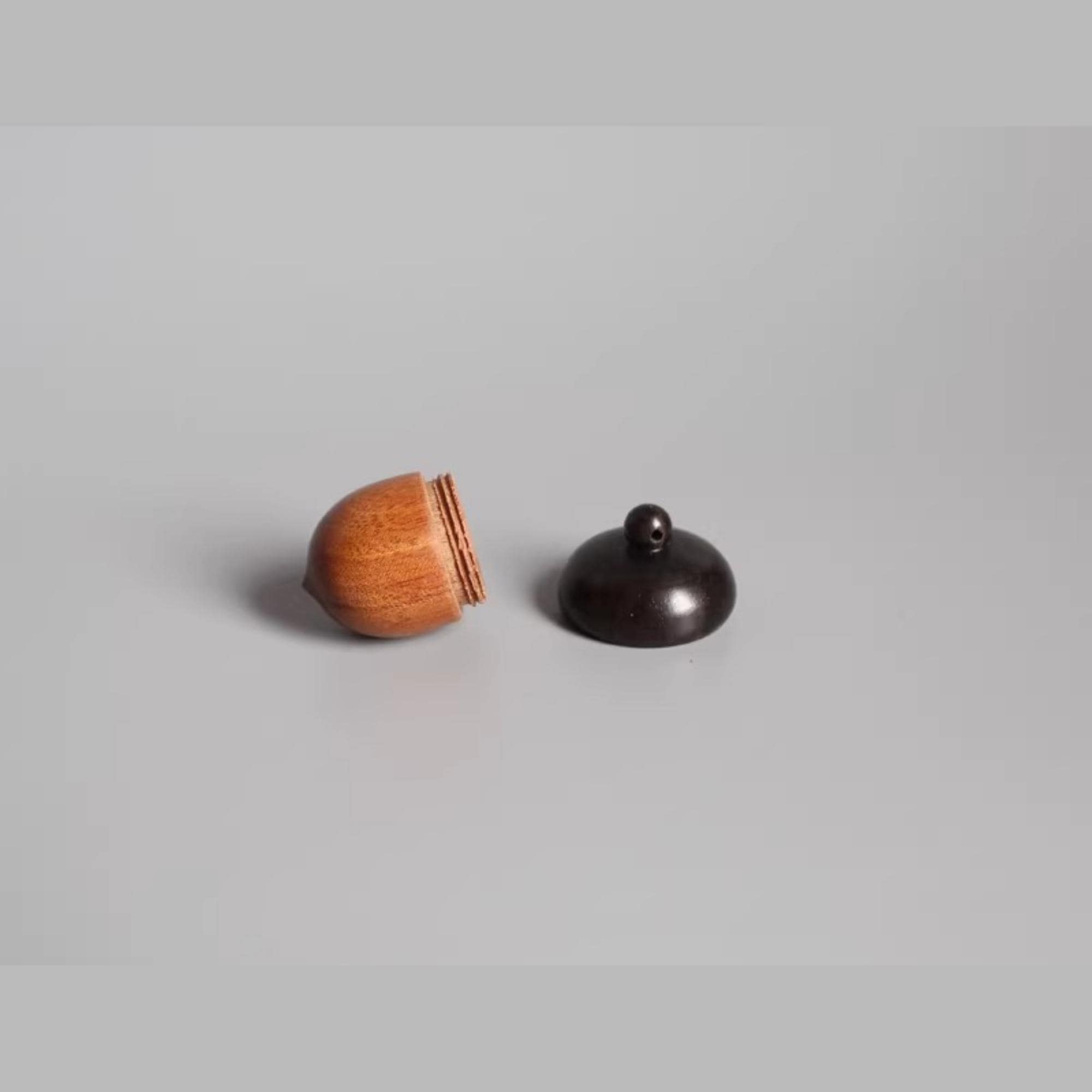 A wooden acorn and a black lid are placed on a plain surface.