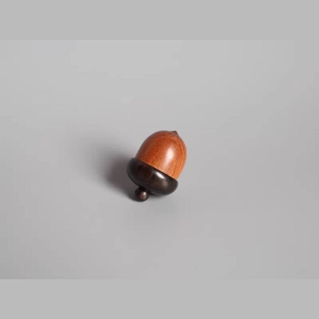 A wooden acorn with a dark brown top and a lighter brown bottom rests on a plain gray background.