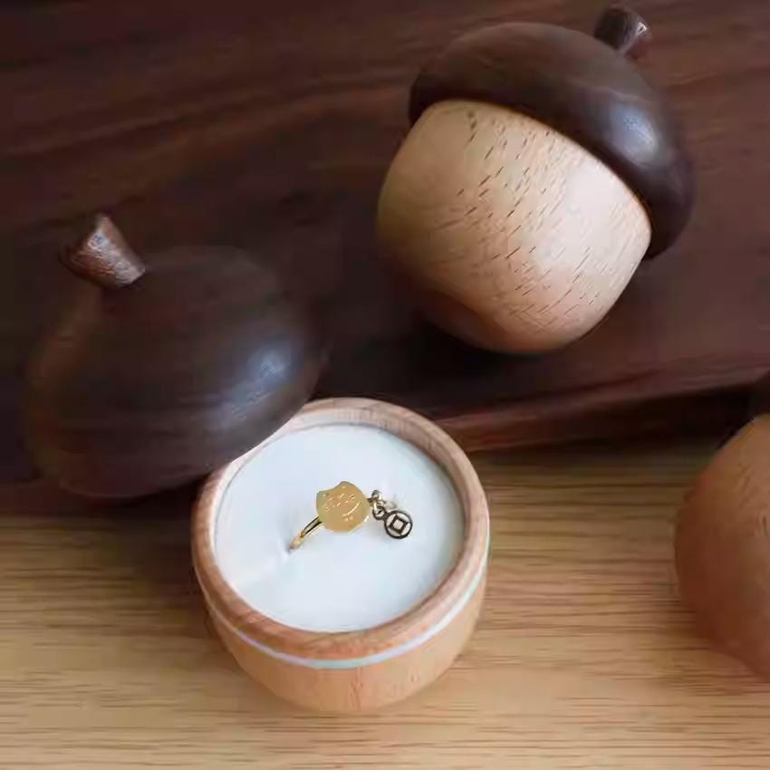 A wooden acorn-shaped container holding a ring with a charm, placed on a wooden surface.