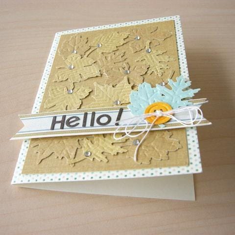 A handmade greeting card with a gold background and leaves, featuring the word "Hello!" written on it.