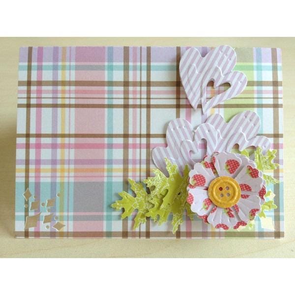 A handmade card with a plaid background, featuring a flower, hearts, and leaves as decorative elements.