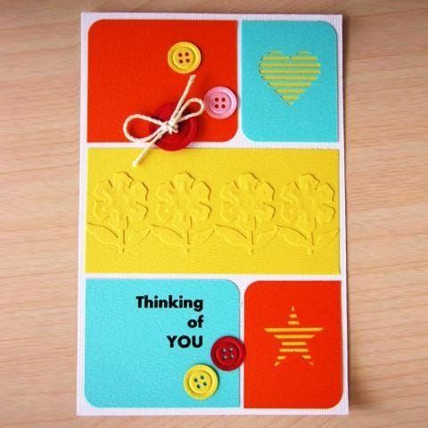 A colorful handmade greeting card with various decorative elements such as buttons, flowers, and a heart shape.