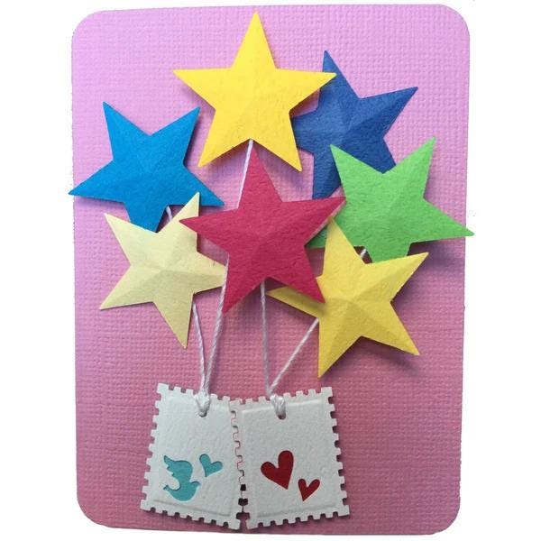 A colorful arrangement of paper stars in various colors, including blue, yellow, green, and red, attached to two white postage stamps with hearts on them, set against a pink background.