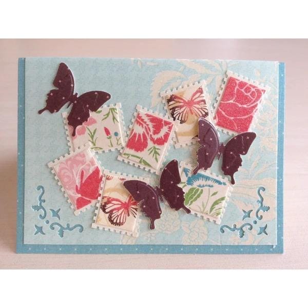 A handmade card featuring a collection of colorful butterfly-shaped cutouts and floral patterns on a light blue background.