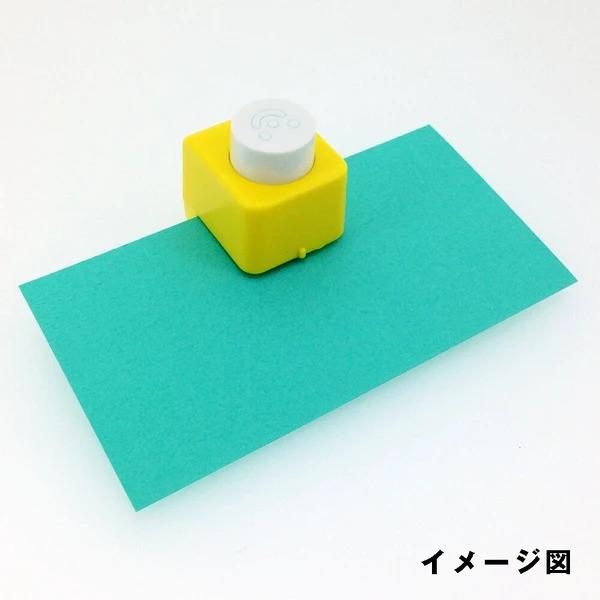 A yellow and white paper punch is placed on a green piece of paper against a white background.