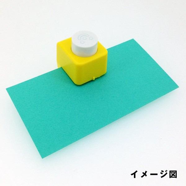 A yellow and white paper punch is placed on a green piece of paper against a white background.