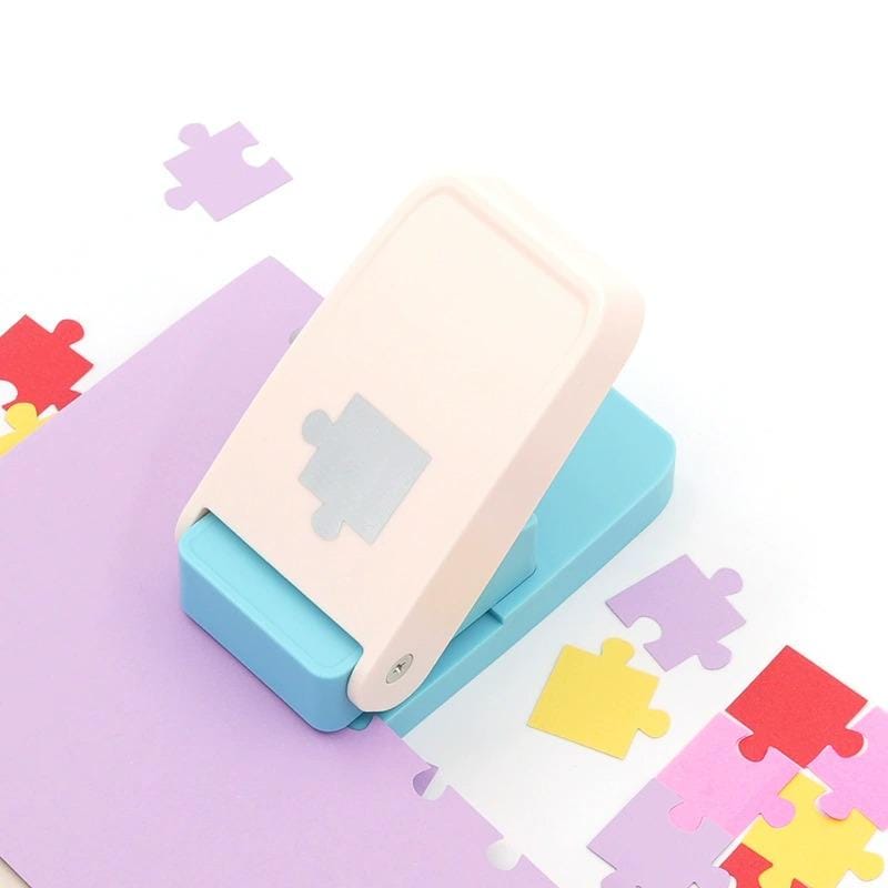 A white and blue paper punch is sitting on a purple surface, surrounded by scattered colorful puzzle pieces.