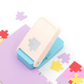 A white and blue paper punch is sitting on a purple surface, surrounded by scattered colorful puzzle pieces.